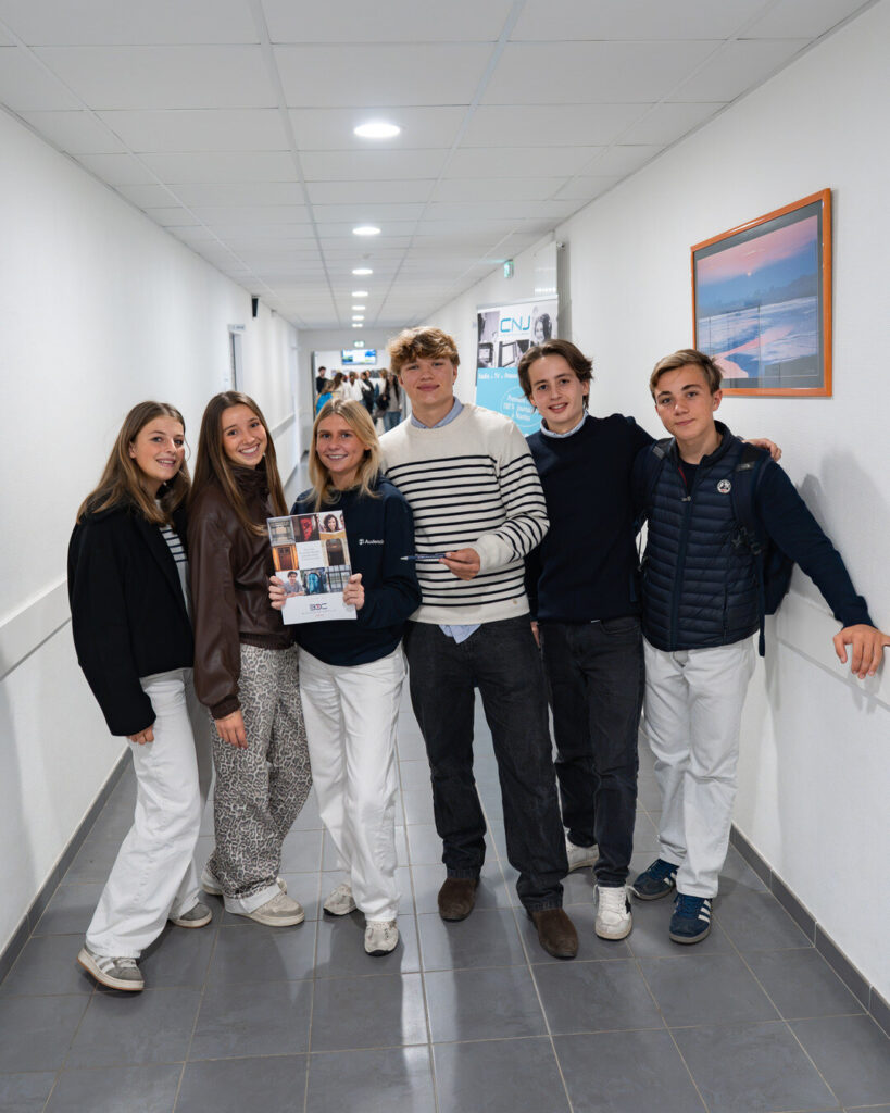 Six élèves posent en souriant dans le couloir du bâtiment lycée ; l'une tient la brochure de la prépa B/L de Blanche de Castille.