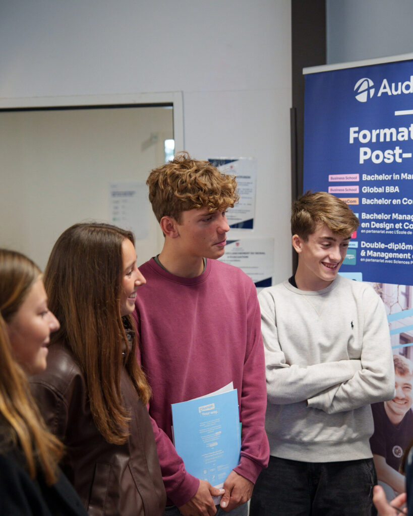 Des lycéens, brochure en main, discutent devant le kakémono « Formations post-bac » d'Audencia.