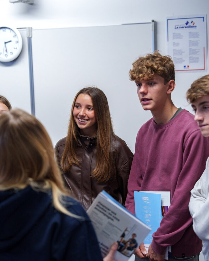 Des lycéens rient, brochures d'Audencia à la main.