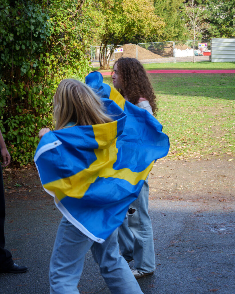 Dans le parc, une élève drapée dans un drapeau suédois danse, de dos, à côté d’une camarade.