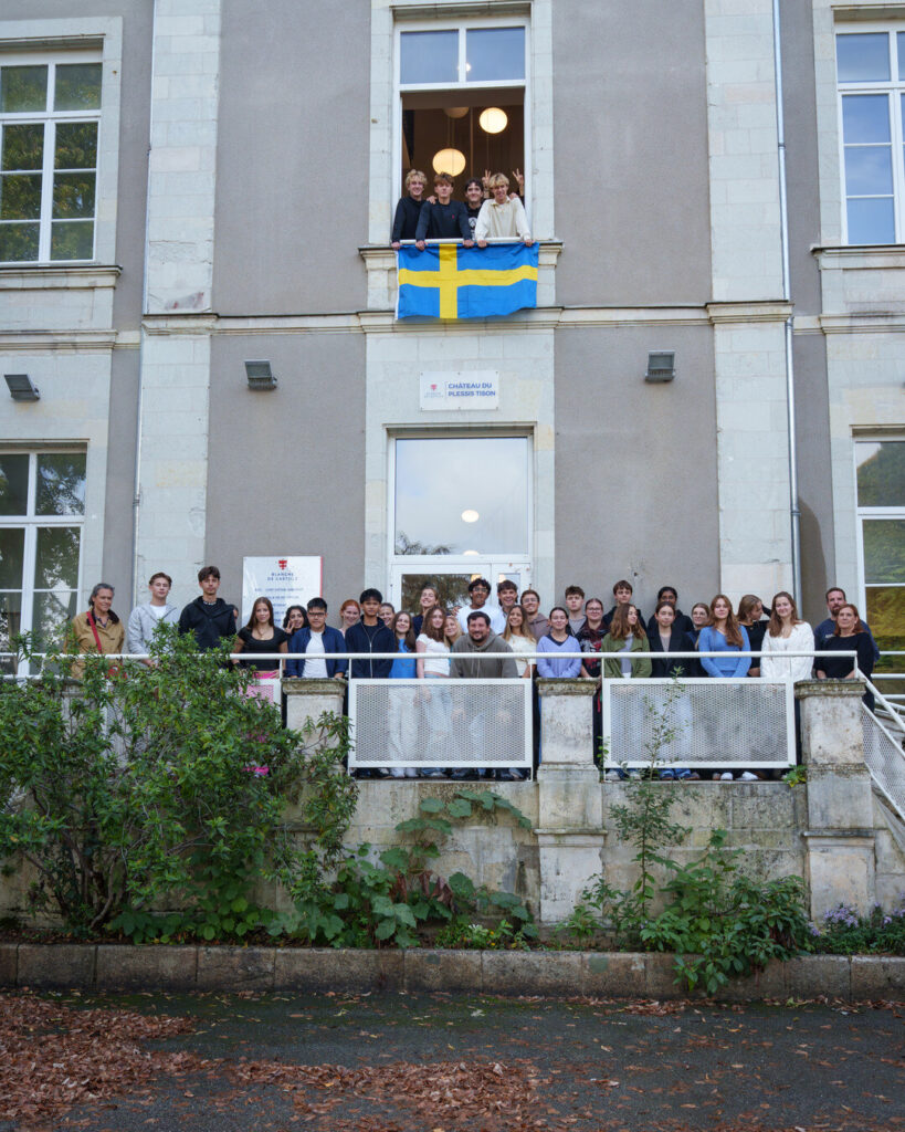 Une quarantaine d’élèves et quelques adultes posent sur le perron du château du Plessis-Tison. Au-dessus, à une fenêtre ouverte, quatre élèves tiennent un drapeau suédois.