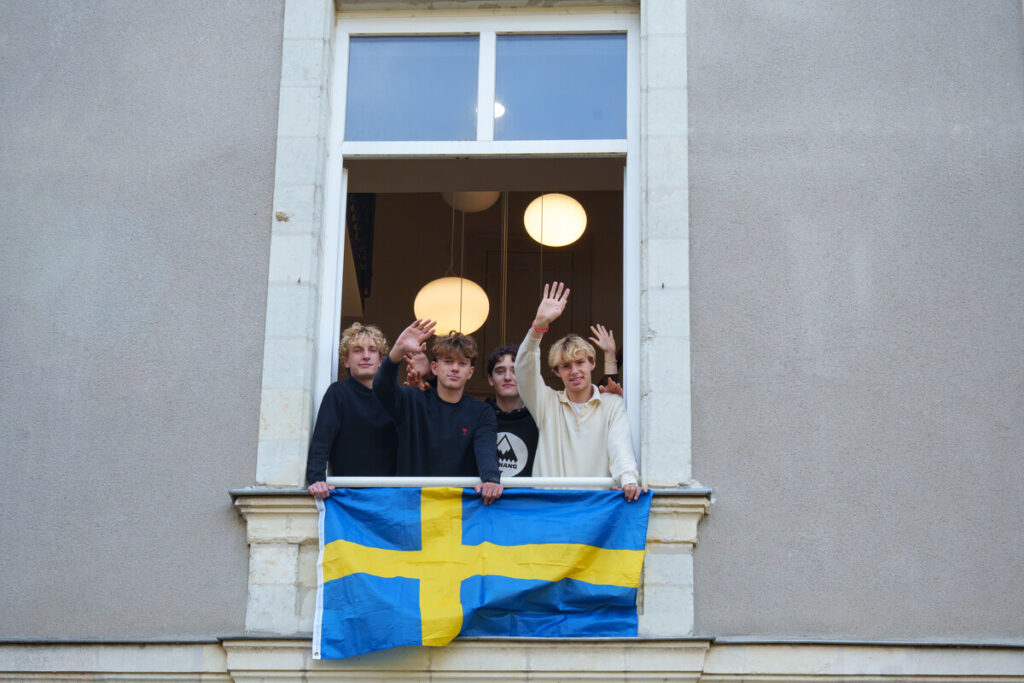 Quatre élèves saluent de la main à une fenêtre du château du Plessis-Tison, un drapeau suédois tendu sur la balustrade.