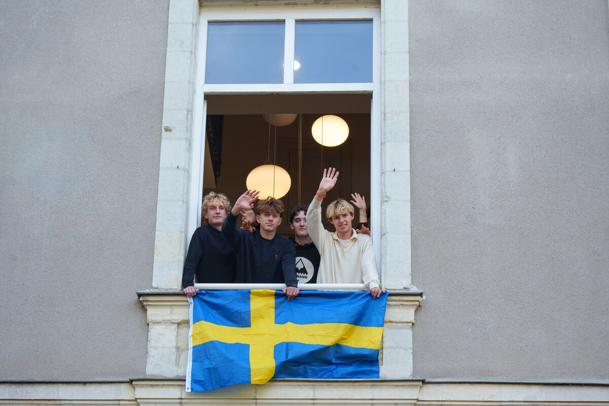Quatre élèves saluent de la main à une fenêtre du château du Plessis-Tison, un drapeau suédois tendu sur la balustrade.